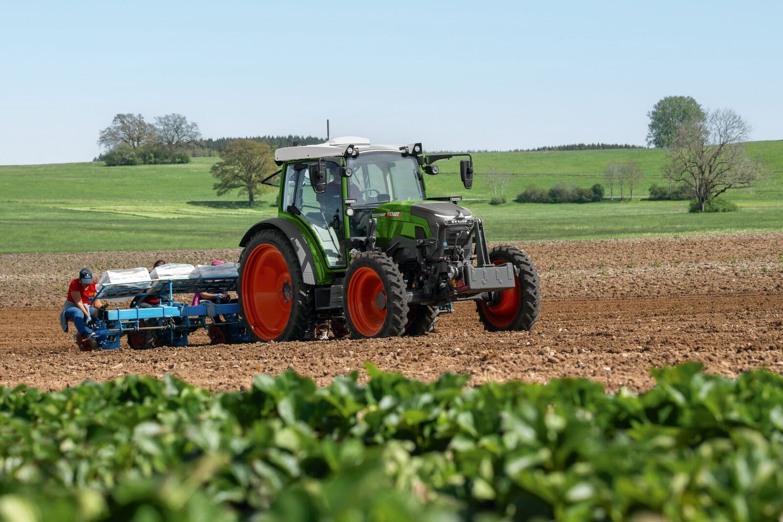 Gesamtansicht des elektrischen Traktors Fendt e107 Vario mit einer Pflanzmaschine bei der Feldarbeit